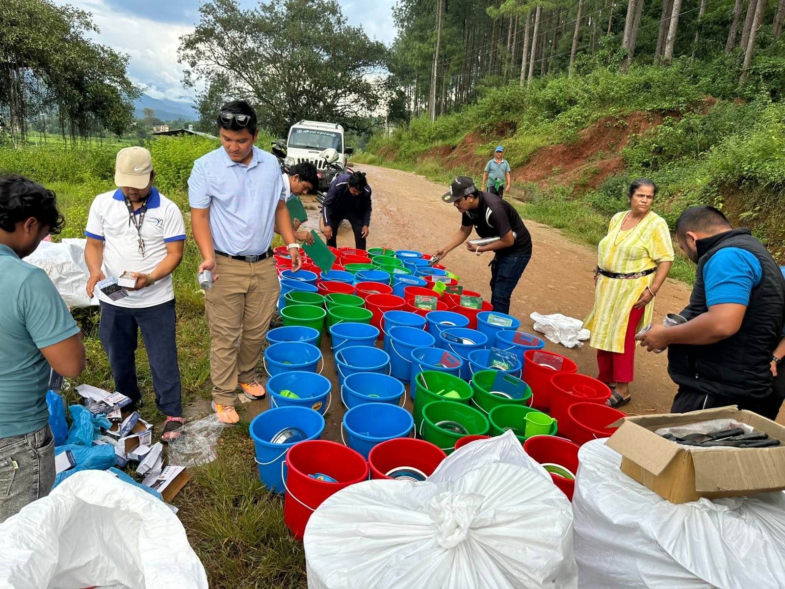 Volunteers assembling bucket kits with utensils along a village road